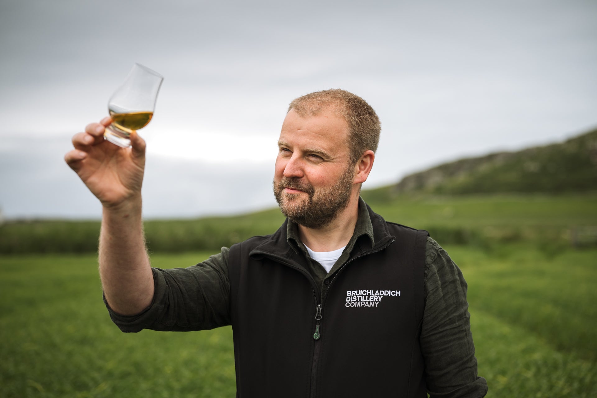 Adam Hannett holding a glass of Bruichladdich The Laddie Rye blended grain islay scotch whisky with a scenic background