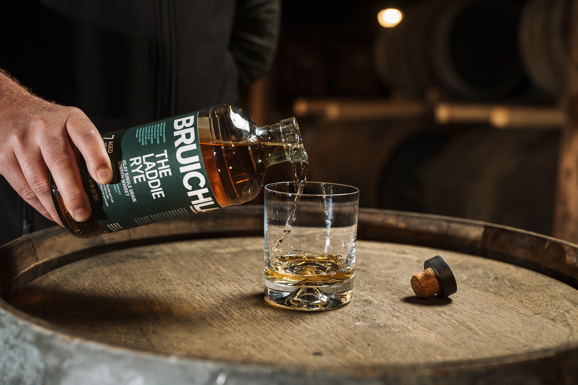 Adam Hannett pouring Bruichladdich The Laddie Rye whisky into a glass on a wooden barrel.